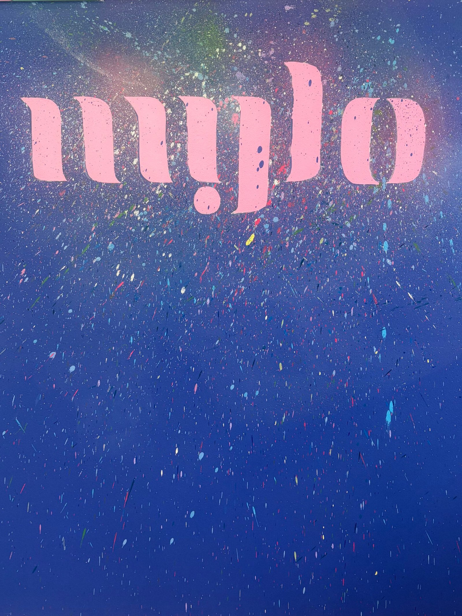L'enseigne MYLO peinte en rose sur un mur bleu tacheté, entourée d'affiches